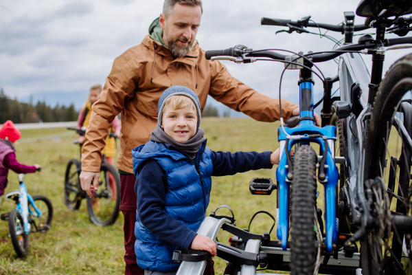 Young family with little children preparing for bicycle ride in nature, putting off bicycles from car racks. Concept of healthy lifestyle and moving activity.