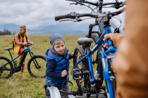 Littlle boy helping father attache a bicycle on bike carrier. Preparing for bicycle ride in nature, putting off bicycles from car racks. Concept of healthy lifestyle and moving activity.