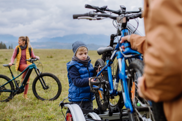 Young family with little children preparing for bicycle ride in nature, putting off bicycles from car racks. Concept of healthy lifestyle and moving activity.