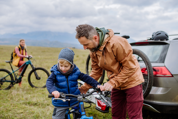 Young family with little children preparing for bicycle ride in nature, putting off bicycles from car racks. Concept of healthy lifestyle and moving activity.