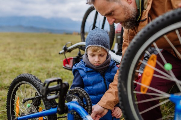 Littlle boy helping father attache a bicycle on bike carrier. Preparing for bicycle ride in nature, putting off bicycles from car racks. Concept of healthy lifestyle and moving activity.