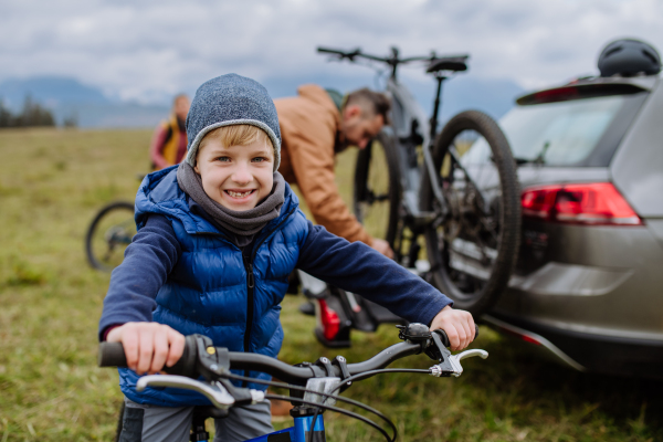 Young boy looking forward to bicycle ride in nature. Father putting off bicycles from car racks. Concept of healthy lifestyle and moving activity.