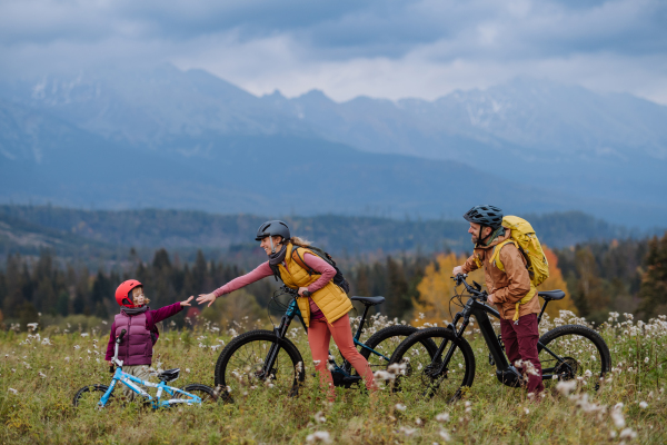 Side view of young family with little daughter at bicycles, in the middle of autumn nature.Concept of healthy lifestyle. Mom and daughter holding hands.