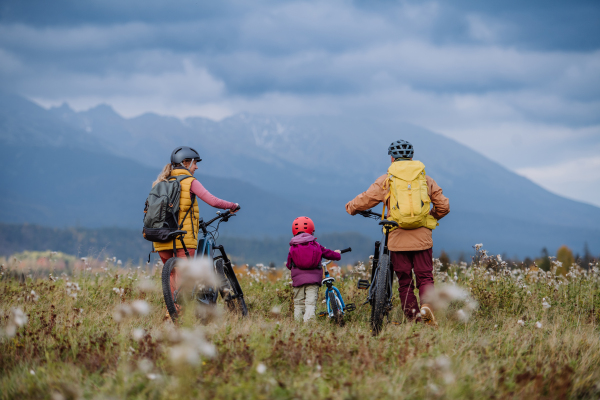 Rear view of young family with little daughter at bicycles, in the middle of autumn nature.Concept of healthy lifestyle.