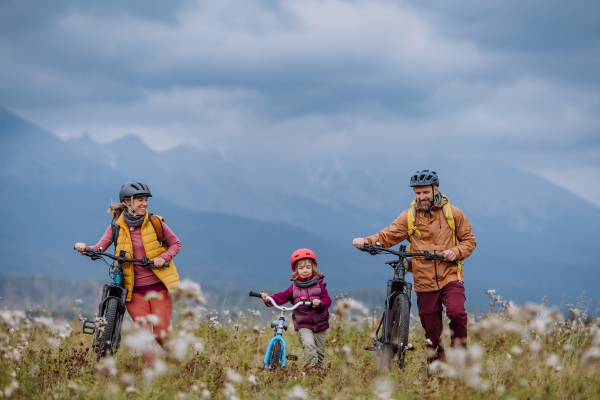 Front view of young family with little daughter at bicycles, in the middle of autumn nature.Concept of healthy lifestyle.