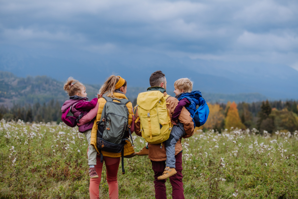 Happy parents with their little kids in arms at autumn walk, in the middle of colourfull nature. Concept of a healthy lifestyle.