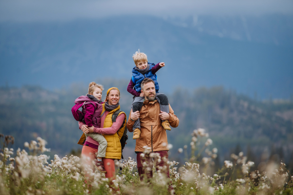 Happy parents with their little kids on piggyback at autumn walk, in the middle of colourfull nature. Concept of a healthy lifestyle. Carrying children on shoulders during the hike.