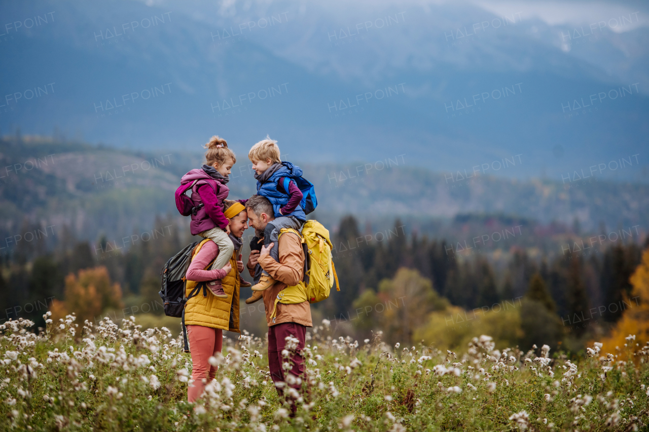 Happy parents with their little kids on piggyback at autumn walk, in the middle of colourfull nature. Concept of a healthy lifestyle.