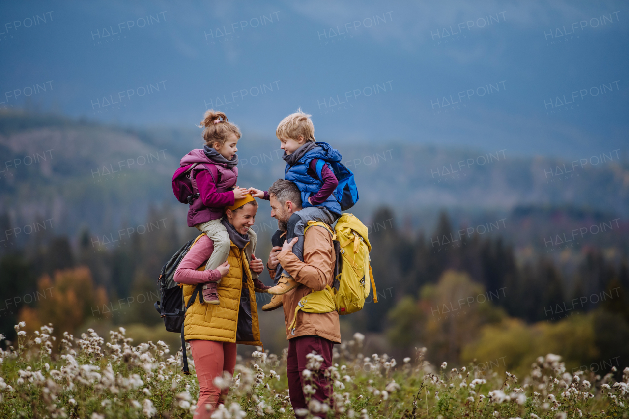 Happy parents with their little kids on piggyback at autumn walk, in the middle of colourfull nature. Concept of a healthy lifestyle. Carrying children on shoulders during the hike.