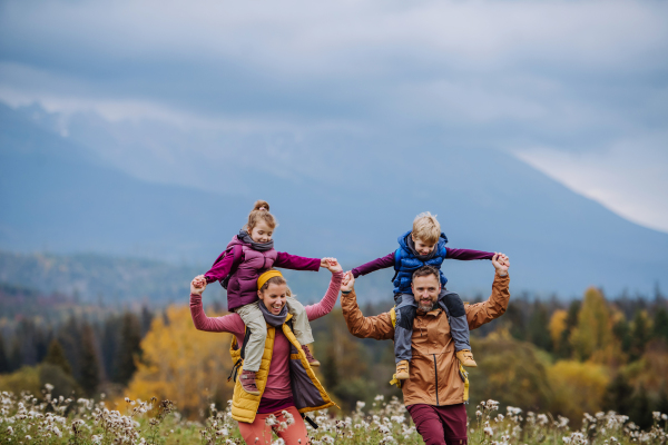 Happy parents with their little kids on piggyback at autumn walk, in the middle of colourfull nature. Concept of a healthy lifestyle. Carrying children on shoulders during the hike.