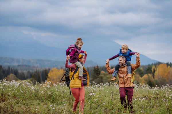 Happy parents with their little kids on piggyback at autumn walk, in the middle of colourfull nature. Concept of a healthy lifestyle.