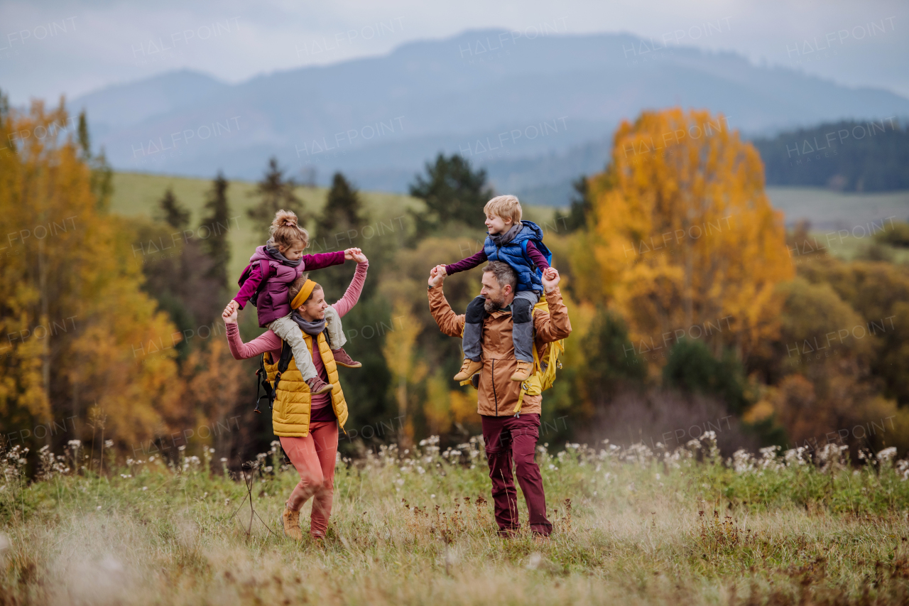 Happy parents with their little kids on piggyback at autumn walk, in the middle of colourfull nature. Concept of a healthy lifestyle.