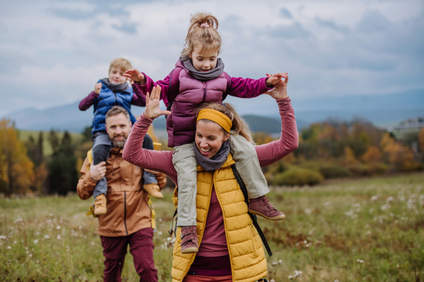 Happy parents with their little kids on piggyback at autumn walk, in the middle of colourfull nature. Concept of a healthy lifestyle. Carrying children on shoulders during the hike.