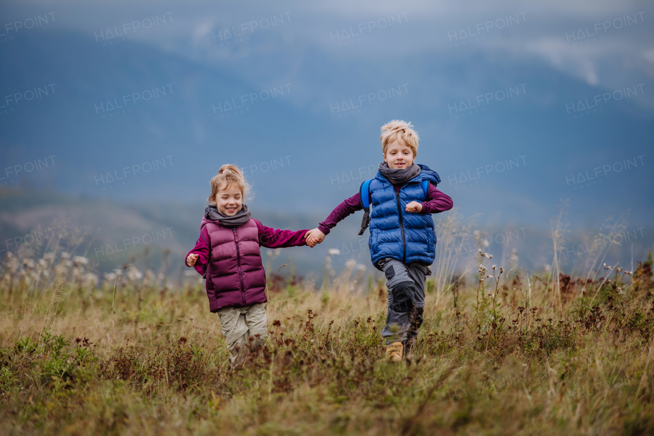 Little children holding each other hands and running at an autumn meadow.