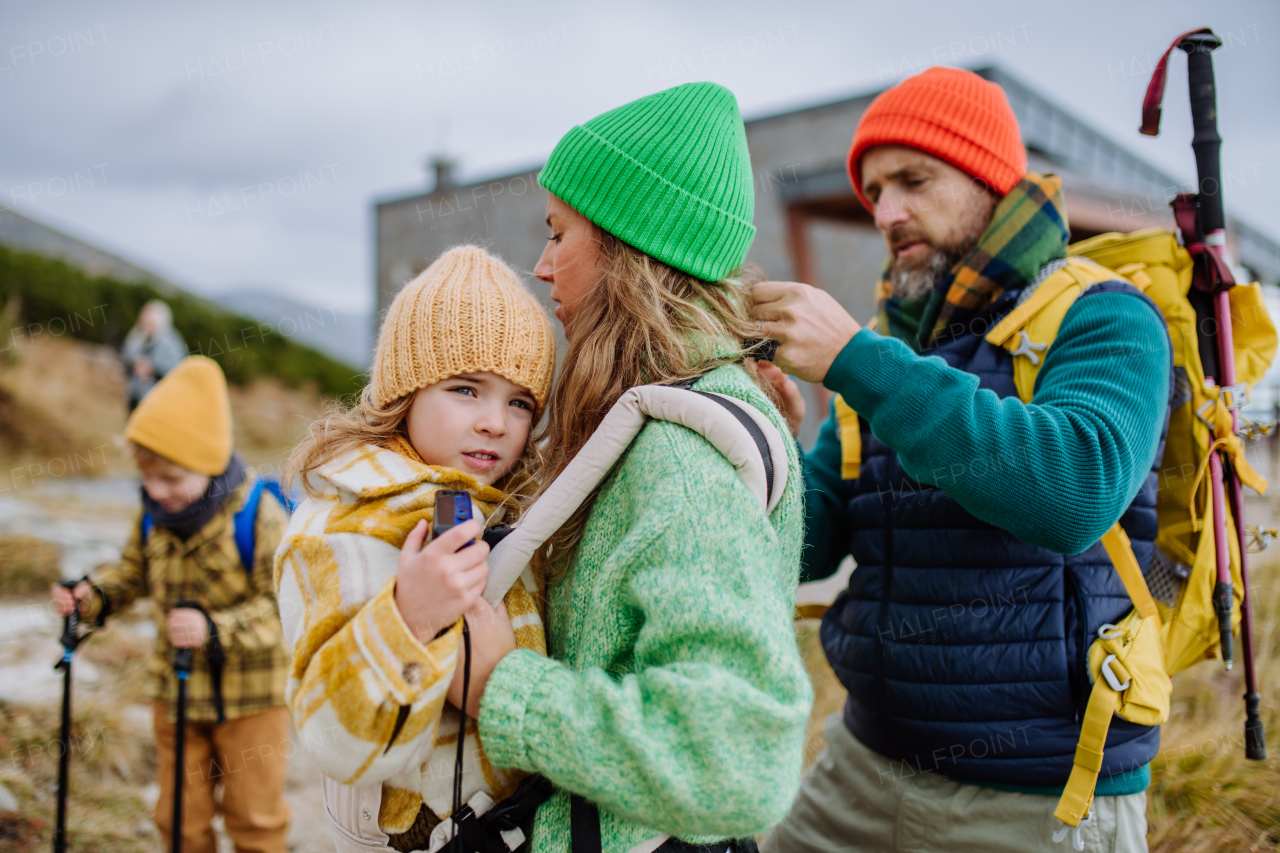 Man helping his wife with their little tired daughter, giving her into child carrier, during autumn hike in the mountains.