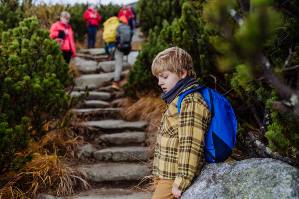 Portrait of tired young boy resting during hard hike in a autumn mountains. Hiking with young kids on difficult terrain.