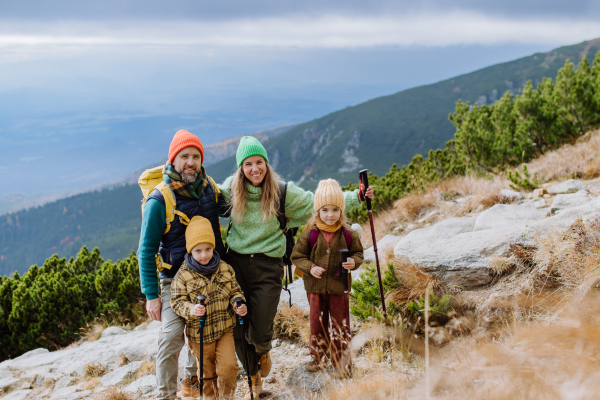 Portrait of happy family with trekkiing poles hiking together in an autumn mountains. Hiking with young kids.