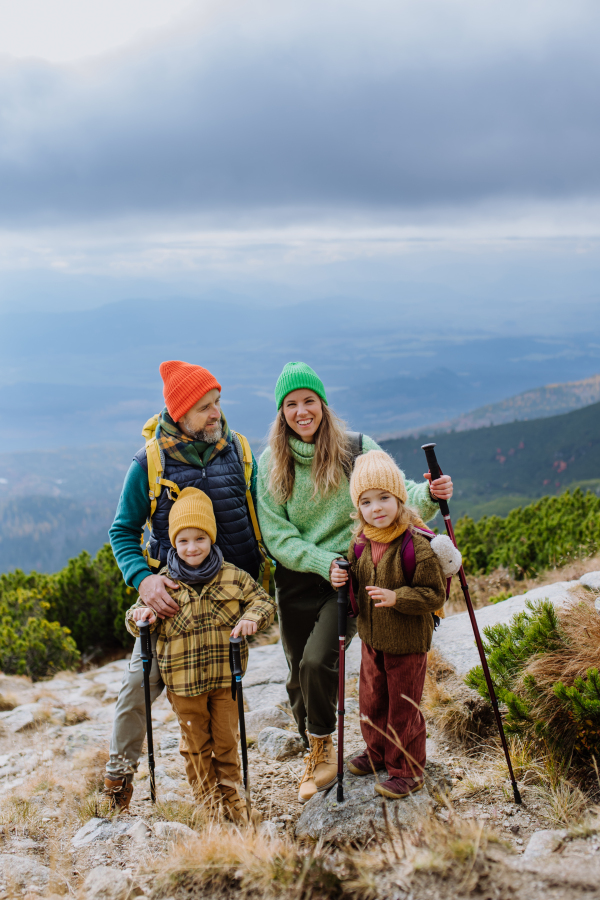 Portrait of happy family with trekkiing poles hiking together in an autumn mountains. Hiking with young kids.