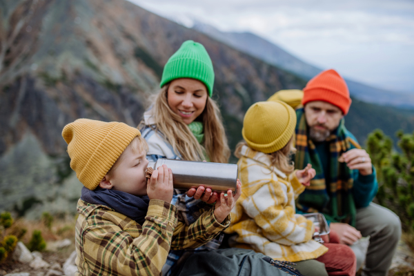 Happy family resting, having snack during hiking together in an autumn mountains. Little boy drinking tea from thermos.