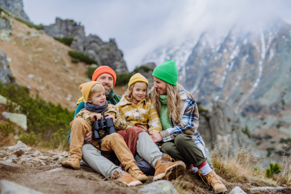 Portrait of happy family resting during long hike in an autumn mountains. Hiking with young kids. Little boy looking through a binoculars.