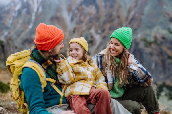 Happy family resting, having snack and enjoying the view during hiking together in an autumn mountains. Mom, dad and daughter on kid friendly hike.