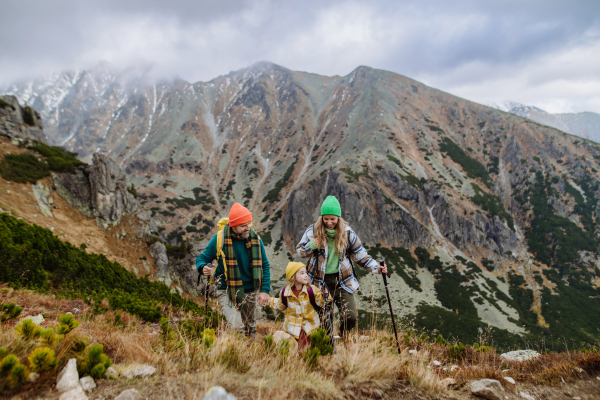 Portrait of happy family of three with trekkiing poles hiking together in an autumn mountains. Hiking with young kids.