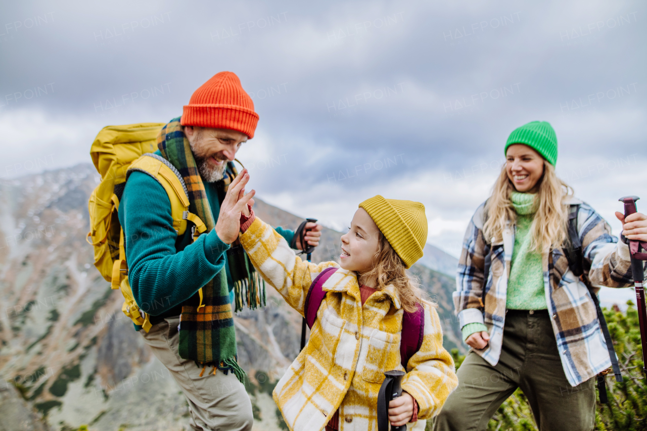 Portrait of happy family of mother, father and daughter on kid friendly hike in an autumn mountains. Dad and little girl giving high five.