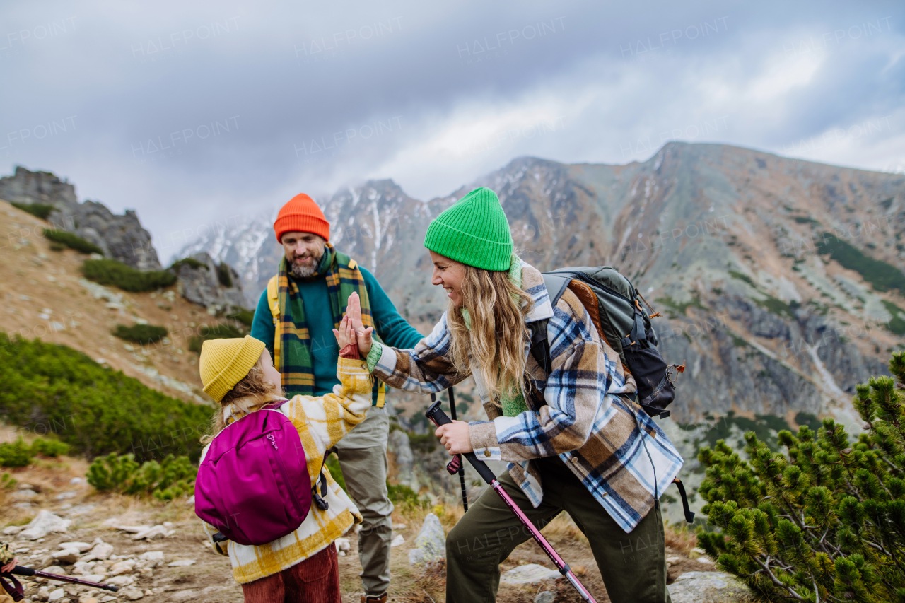 Portrait of happy family of mother, father and daughter on kid friendly hike in an autumn mountains. Mom and little girl giving high five.