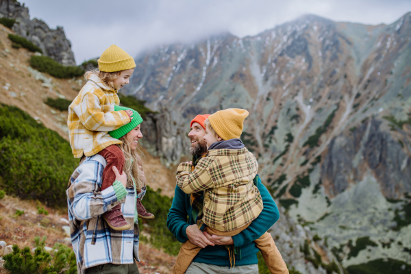 Portrait of happy family hiking together in an autumn mountains. Hiking with young kids. Mother carrying young girl on shoulders.