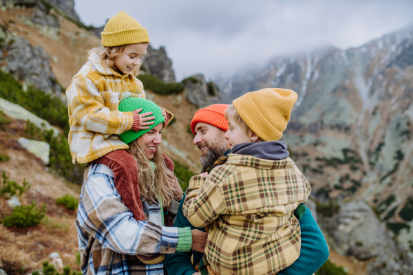 Portrait of happy family hiking together in an autumn mountains. Hiking with young kids. Mother carrying young girl on shoulders.