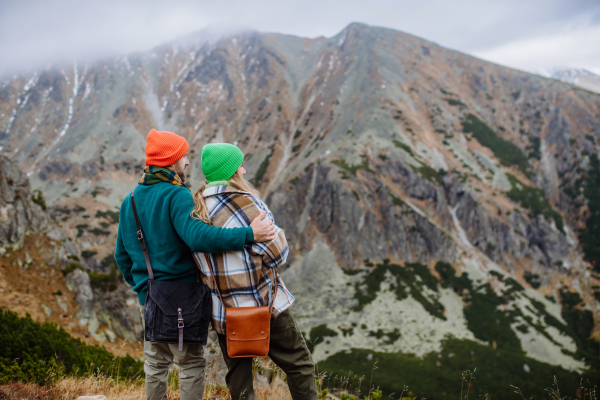 Rear view of young happy couple at a mountain hike, hugging each other. Married couple spending their honeymoons hiking, backpacking, visiting national parks.