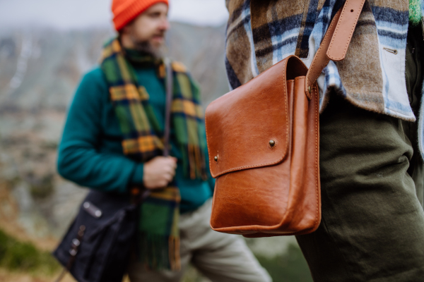 Close-up of a leather crossbody bag. Woman weraring crossody bag during the hike in an autumn mountains. Hikers carrying gear in shoulder bags on hike.