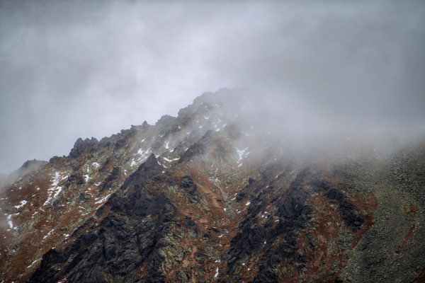 View of mountain peak in fog. Beautiful landscape of mountain with high rocks in low clouds.