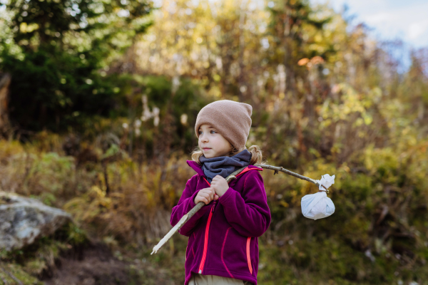 Portrait of little girl with bindle during autumn hike in mountains. Girl holding stick with cloth carrying snack inside.