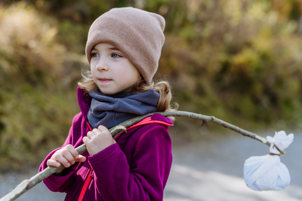 Portrait of little girl with bindle during autumn hike in mountains. Girl holding stick with cloth carrying snack inside.