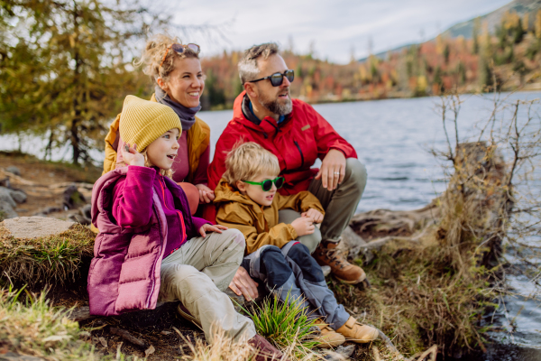 Happy young family with little children, resting near a lake in mountains.