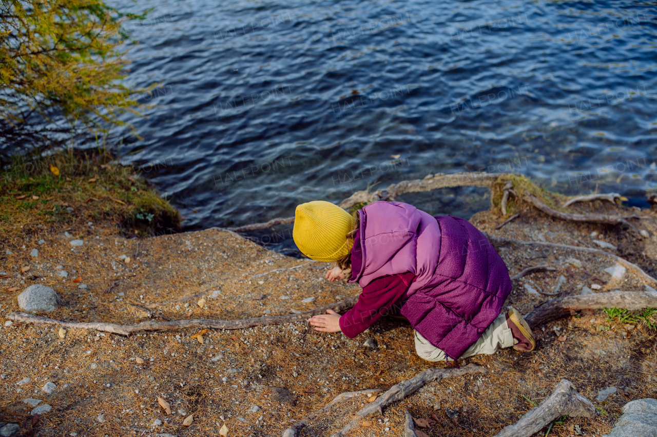 Little girl playing on the shore of the lake in mountains. Girl tourist resting near the lake, having fun and playing with pebbles.