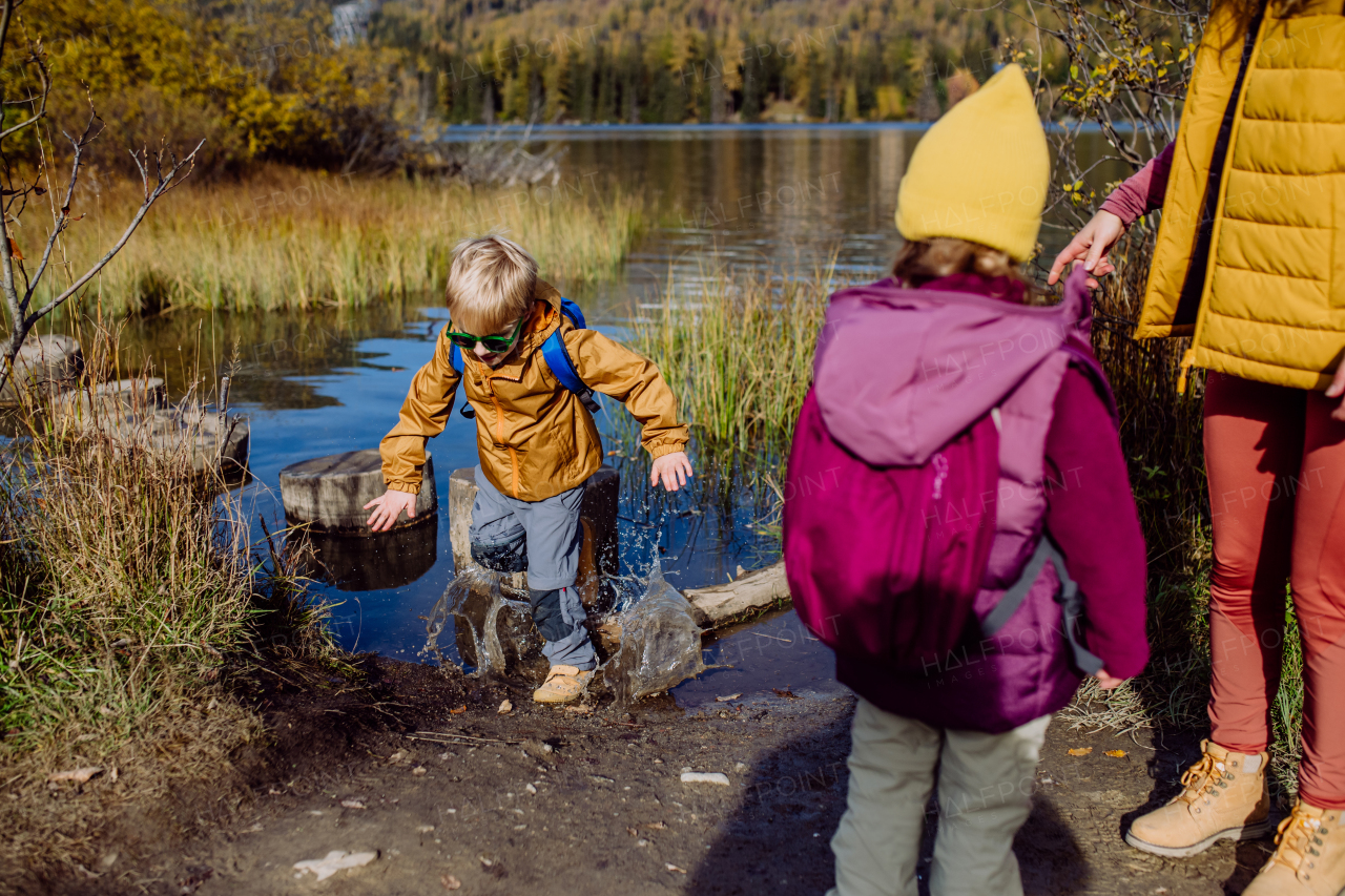 Little boy slipping on wet shore around the lake. Falling in water in the middle of hike.