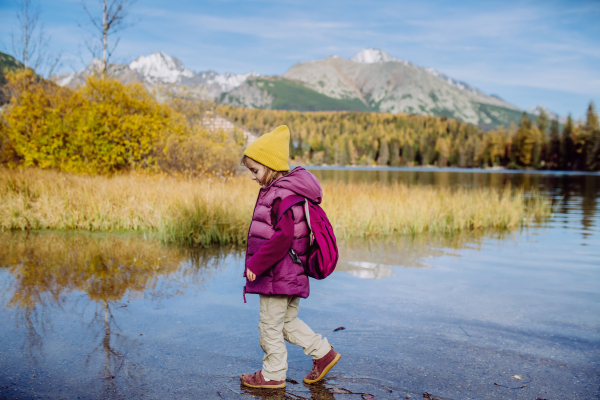 Little girl walking in shore of lake, in the middle of beautiful autumn nature.