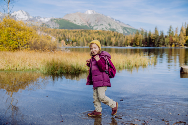 Little girl walking in shore of lake, in the middle of beautiful autumn nature.