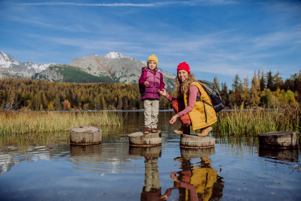 Mother with daughter standing on wooden steps on the shore of the lake in mountains. Female tourist with little kid enjoying mountains view.