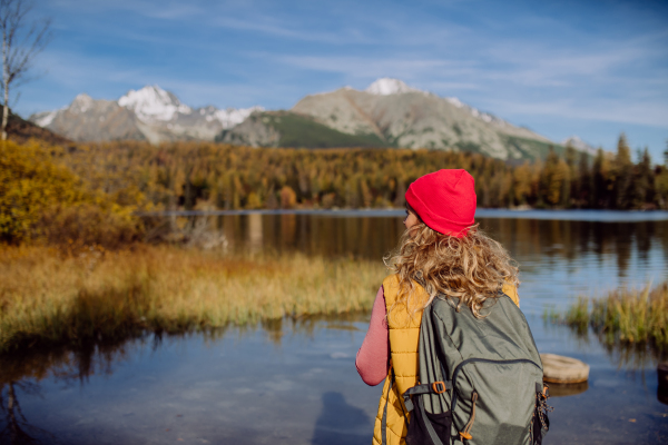 Rear view of woman standing on the shore of the lake in mountains. Female tourist enjoying mountains view.