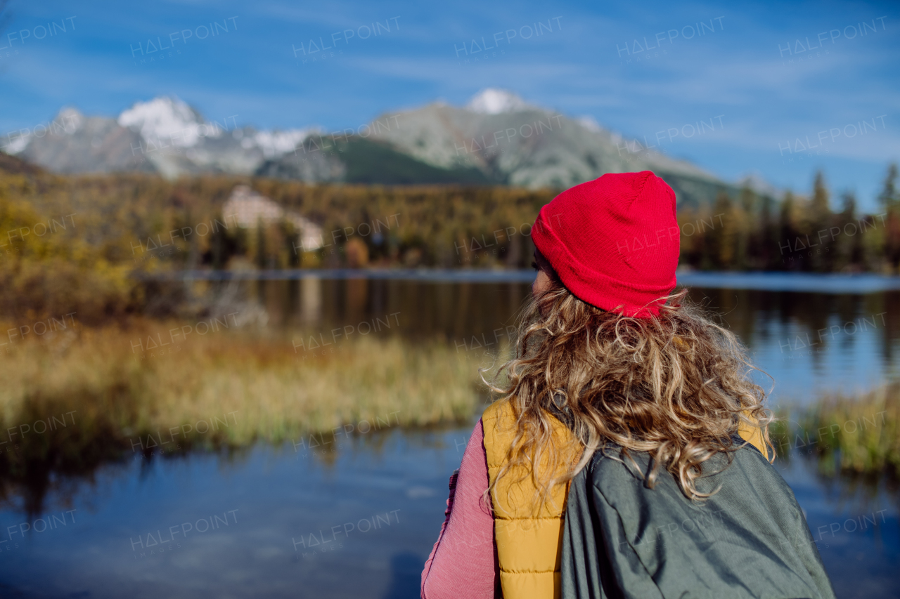 Rear view of woman standing on the shore of the lake in mountains. Female tourist enjoying mountains view.