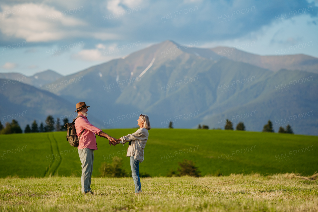 Senior couple standing in the middle of meadow and having romantic moment at the autumn nature. Elderly spouses looking at serene landscape, enjoying beautiful view at High Tatras. Minimalist landscape photography with copy space.