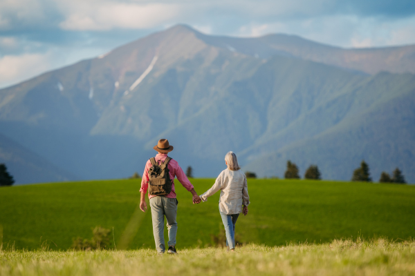 Senior couple standing in the middle of meadow and having romantic moment at the autumn nature. Elderly spouses looking at serene landscape, enjoying beautiful view at High Tatras. Minimalist landscape photography with copy space.