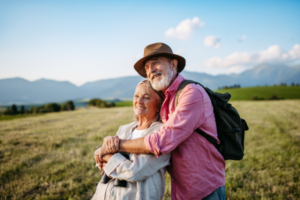 Potrait of senior couple sitting at meadow and having romantic moment at the autumn nature. Elderly spouses embracing each other with serene landscape of High Tatras behind them.