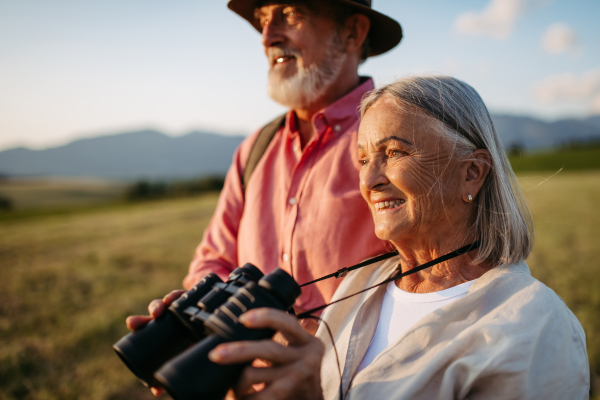 Portrait of a senior woman looking through binoculars. Senior couple walking through the autumn nature. Elderly spouses going mushroom picking.