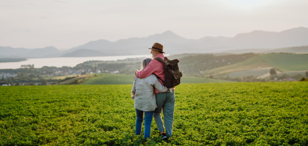 Senior couple standing in the middle of meadow and having romantic moment at the autumn nature. Elderly spouses looking at serene landscape, enjoying beautiful view at High Tatras. Minimalist landscape photography, banner with copy space.