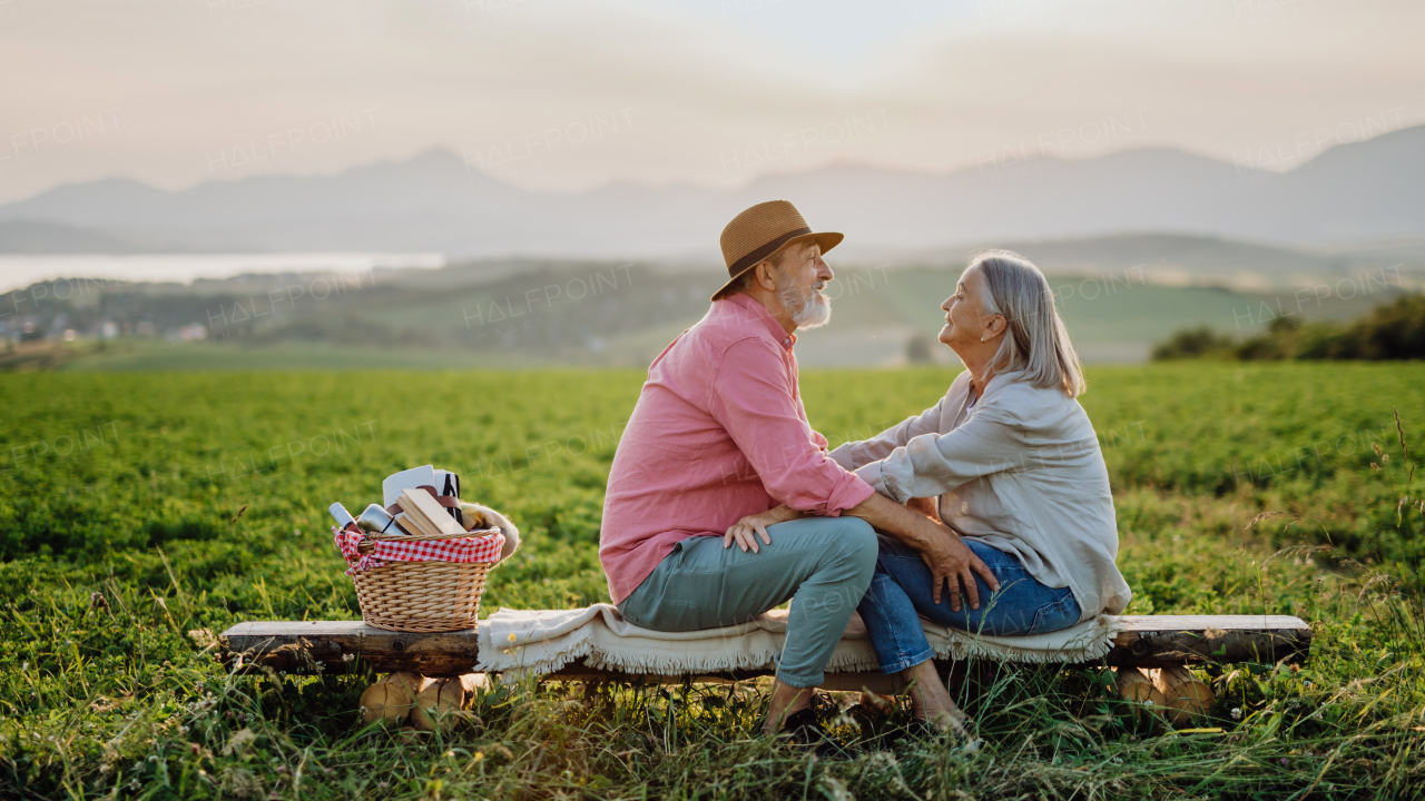 Senior couple sitting at meadow and having romantic moment at the autumn nature. Elderly spouses looking at each other with serene landscape of High Tatras behind them.