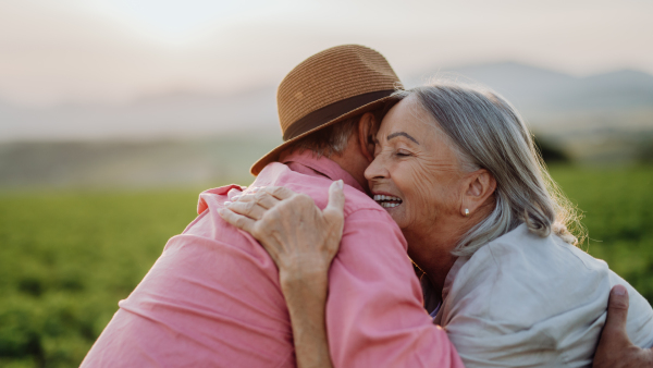 Potrait of senior couple sitting at meadow and having romantic moment at the autumn nature. Elderly spouses embracing each other with serene landscape of High Tatras behind them.